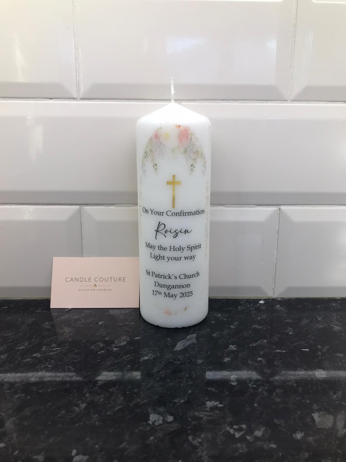A white candle with floral patterns and personalized text including the name 'Regina' and a date. There is a cross symbol on the candle, indicating its use for religious ceremonies.