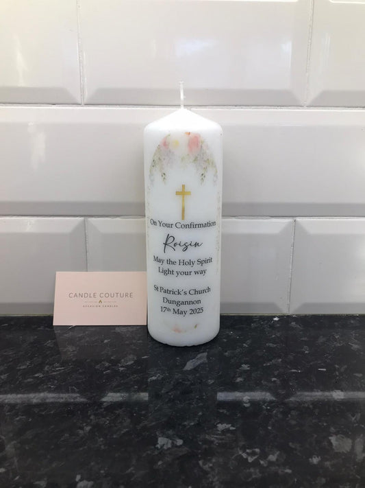 A white candle with floral patterns and personalized text including the name 'Regina' and a date. There is a cross symbol on the candle, indicating its use for religious ceremonies.